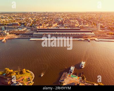 Vista aerea sulla stazione ferroviaria centrale di Amsterdam e sul fiume IJ ad Amsterdam nei Paesi Bassi intorno al tramonto Foto Stock