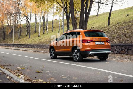 Vista posteriore di tre quarti del crossover samoa Orange SEAT Ateca. Giorno nuvoloso d'autunno sulla strada del parco di campagna Foto Stock