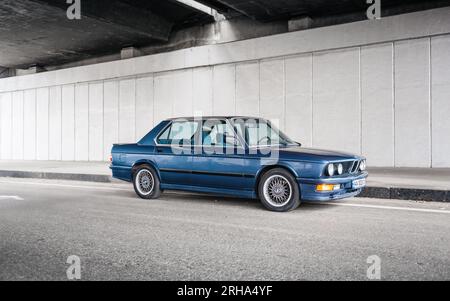 Blu scuro BMW serie 5 E28 parcheggiata sotto il ponte. Guidare una vecchia auto in un fine settimana. Foto Stock
