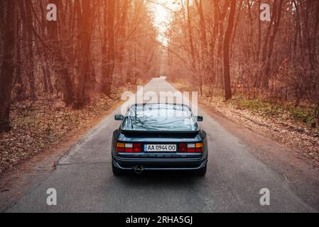 Videogame di corse ma nella vita reale: Porsche 944 blu scuro su una strada stretta attraverso una foresta. Mi piaceva giocare a NFS quando era piccolo, ora ricreando momenti Foto Stock