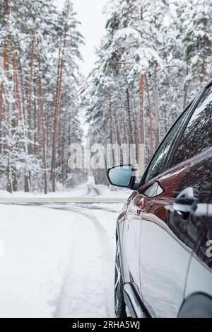 vista laterale di un'auto marrone che guida su una strada innevata nella pineta, in prossimità dell'incrocio con una strada a doppio senso. Foto Stock