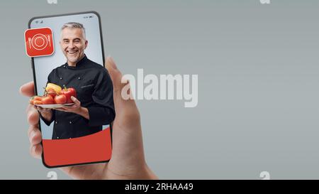 Chef sorridente sullo schermo dello smartphone: Assumi professionisti online e cucina su richiesta Foto Stock