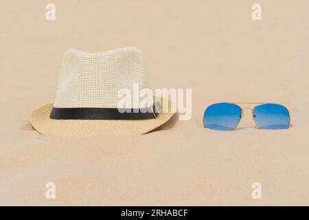 Gli occhiali da sole blu e un cappello leggero si trovano sulla sabbia. Vacanze estive, viaggi e turismo. Riposo estivo. Stagione natalizia Foto Stock
