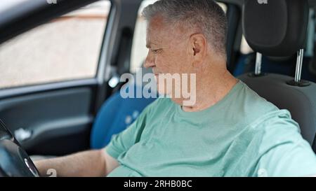 Uomo dai capelli grigi di mezza età sorridente che inizia l'auto in strada Foto Stock