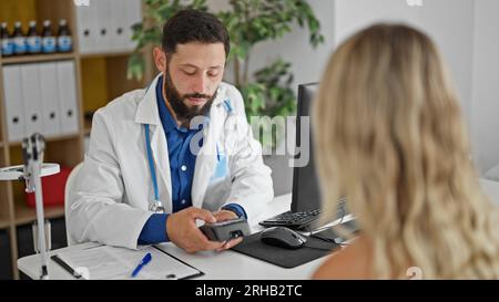 Giovane uomo ispanico medico che carica visita medica al paziente presso la clinica Foto Stock