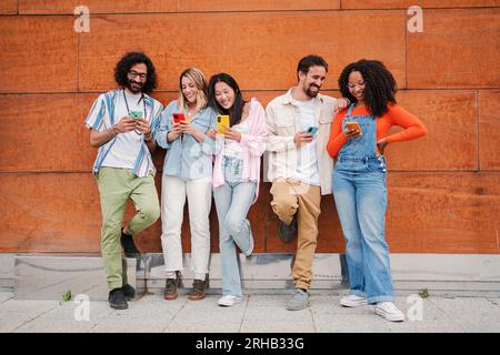 Un gruppo sorridente di giovani amici che utilizzano o guardano il cellulare, condividendo momenti divertenti sull'app dei social media. Persone felici che inviano messaggi di testo o navigano su Internet con il loro smartphone insieme. Foto di alta qualità Foto Stock