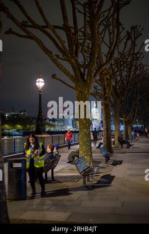 LONDRA - 22 aprile 2023: Fascino notturno a Southbank, gente tra alberi e panchine. La cattedrale di St Paul brilla sullo sfondo. Foto Stock