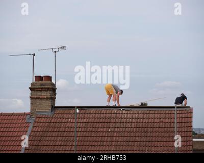 Costruttori che lavorano sul tetto della proprietà a Londra contro il cielo blu Foto Stock