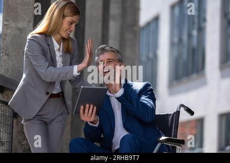 Due persone d'affari che danno cinque, progetto di completamento celebrativo, uomo in sedia a rotelle. Foto Stock