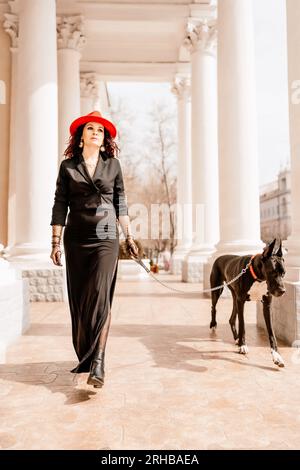 Una foto di una donna e della sua Grande Dane che cammina per una città, ammirando le immagini e i suoni dell'ambiente urbano. Foto Stock