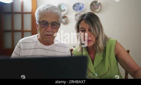 Coppia anziana in difficoltà, che parla di problemi finanziari a casa di fronte a un computer portatile. Sconvolta marito e moglie che litigano per la multa per l'auto, pagando de Foto Stock