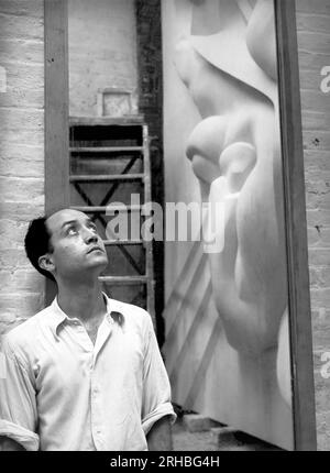 New York, New York: 1940 Isamu Noguchi con un riflesso della placca dell'Associated Press Building, scolpita in gesso e fusa in acciaio inossidabile - all'epoca la più grande fusione di acciaio inossidabile di sempre. È ancora installato nel Rockefeller Center. Foto Stock