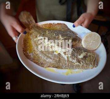 Primo piano di una donna che tiene un piatto con rombo cotto al momento e limone Foto Stock