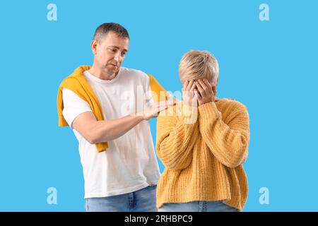 Piange una donna matura con suo marito dopo una lite su sfondo blu Foto Stock