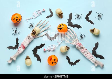 Composizione con mani scheletriche, teschi, zucche, pipistrelli di carta e ragni per festeggiare Halloween su sfondo blu Foto Stock