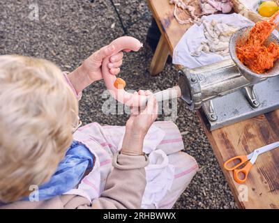 Alto angolo di anziana lavoratrice femminile irriconoscibile che ripieno intestino da tritacarne sul tavolo in campagna Foto Stock