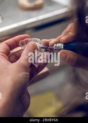 Dall'alto di un ortodontista maschile anonimo che utilizza una macchina rotativa per la lucidatura della bocca di protezione in un laboratorio odontoiatrico professionale Foto Stock