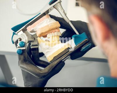 Vista posteriore di un dentista sfocato e irriconoscibile in guanti che reggono lo strumento mentre si lavora sulla mascella durante le protesi dentali Foto Stock