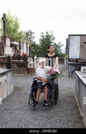 ragazza con donna disabile che porta fiori al cimitero Foto Stock