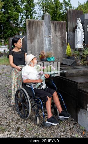 ragazza con donna disabile che porta fiori al cimitero Foto Stock