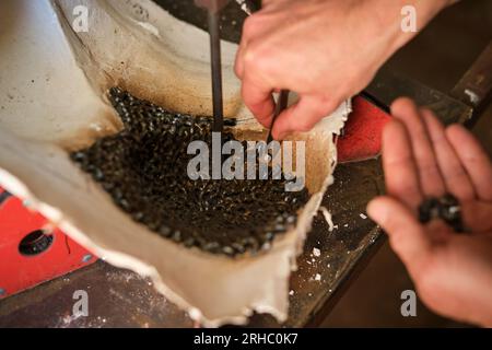 Dal lato superiore del raccolto, artigiano anonimo che sistemano pezzi metallici nello stampo per la saldatura presso il banco di lavoro in officina Foto Stock