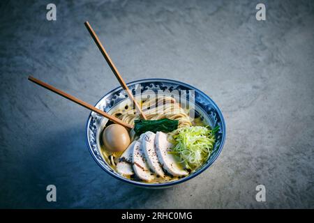 Dall'alto della zuppa asiatica yummy con tagliatelle cotte e pezzi di pollame con verdure fresche e bastoncini di pollo su sfondo grigio Foto Stock