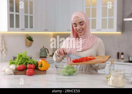 Donna musulmana che prepara una deliziosa insalata con verdure al tavolo bianco in cucina Foto Stock