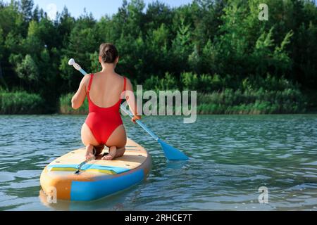 Donna che si imbarca su una tavola SUP nel fiume, vista sul retro Foto Stock