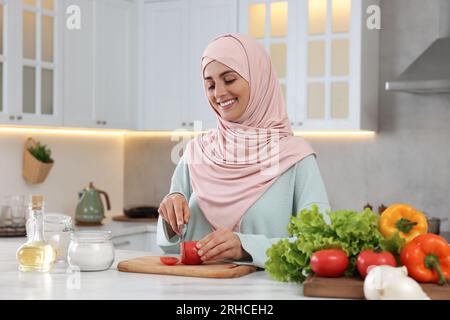 Donna musulmana che prepara una deliziosa insalata con verdure al tavolo bianco in cucina Foto Stock