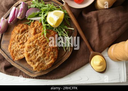 Gustosi schnitzels serviti con cipolla, limone e microgreen su un tavolo di legno bianco, piatti Foto Stock