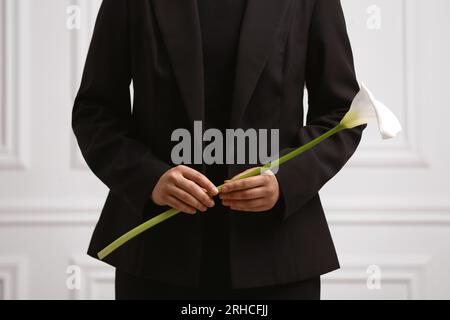 Donna con fiore di giglio di calla vicino al muro bianco, primo piano. Cerimonia funebre Foto Stock