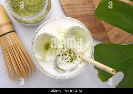 Bicchiere di gustoso latte matcha freddo, foglie, polvere e frusta di bambù su un tavolo bianco Foto Stock