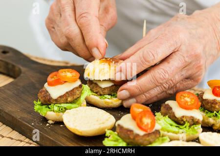 Mettere uno stuzzicadenti sull'hamburger. Preparazione passo-passo dei mini hamburger. Mini hamburger fatti in casa per bambini o antipasti. Piccoli hamburger. Assemb Foto Stock