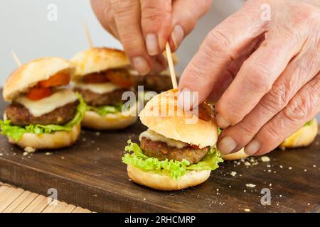 Mettere uno stuzzicadenti sull'hamburger. Preparazione passo-passo dei mini hamburger. Mini hamburger fatti in casa per bambini o antipasti. Piccoli hamburger. Assemb Foto Stock