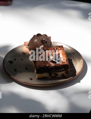 brownie al cioccolato con neve e gocce di cioccolato, piatto in ceramica su un tavolo bianco con luce naturale Foto Stock