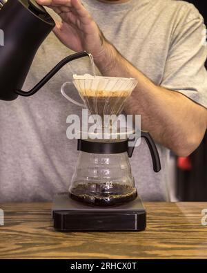 caffè speciale con un v60 estratto con acqua bollente e tazza in ceramica nera, tavolo in legno massello Foto Stock