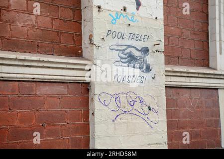 Poster stradale con puntini con testo, tavolo da biliardo, tostie. Graffiti su un vecchio muro di mattoni rossi in Grey Street St Kilda. Foto Stock