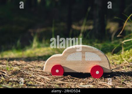 Macchinina giocattolo in legno su sfondo verde della foresta. Eco-car Concept World auto giorno libero veicolo elettrico ambiente trasporto auto elettrico. Ibrido elettrico. Motore sostenibile. Zero emissioni di CO2 per la consapevolezza naturale e il concetto di inquinamento ambientale verde Foto Stock