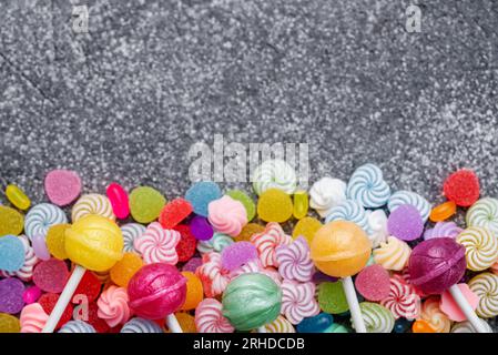 Lollipop e caramelle dolci colorate su fondo di cemento nero. Piano di giacitura, vista dall'alto Foto Stock