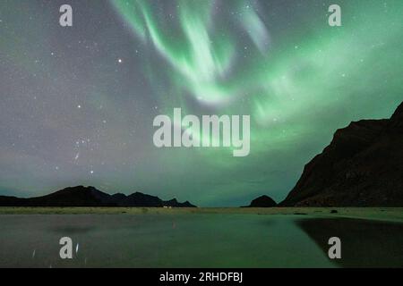 Le luci verdi dell'aurora boreale si riflettono nel mare freddo, nell'Haukland, nella contea del Nordland, nelle isole Lofoten, in Norvegia Foto Stock