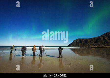 I fotografi si divertono a guardare l'aurora boreale in piedi sulla spiaggia di Skagsanden, Ramberg, Isole Lofoten, Norvegia Foto Stock