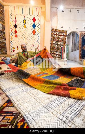 Uomo che mostra tappeti in un mercato baazar, montagne dell'Atlante, provincia di Ouarzazate, Marocco Foto Stock