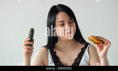 La donna dai capelli neri sceglie tra cibo fresco e fast food Foto Stock