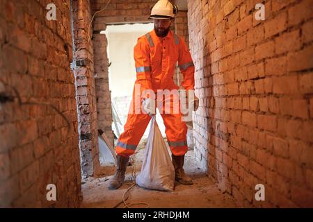 Operaio edile che trasferisce manualmente i rifiuti in sacchetti di zucchero in loco. Foto Stock