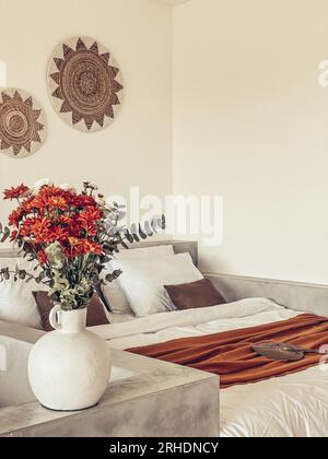 Bouquet di crisantemi d'arancia con foglie di eucalipto vicino al letto con bedrunner di terracotta Foto Stock