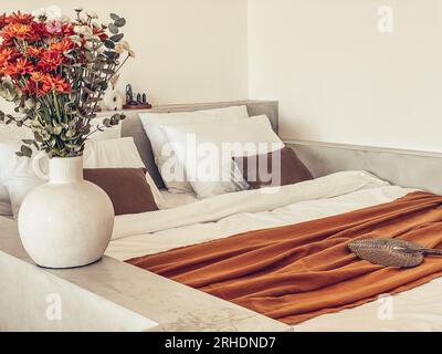 Bouquet di crisantemi d'arancia con foglie di eucalipto vicino al letto con bedrunner di terracotta Foto Stock