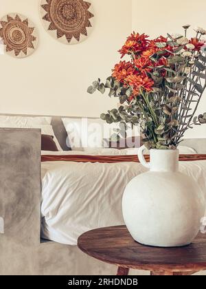 Bouquet di crisantemi d'arancia con foglie di eucalipto vicino al letto con bedrunner di terracotta Foto Stock
