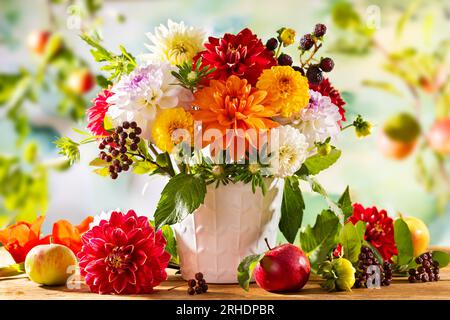 Natura morta autunnale con fiori da giardino. Bellissimo bouquet autunnale in vaso, mele e frutti di bosco su un tavolo di legno. dahlia colorata e crisantemo. Foto Stock