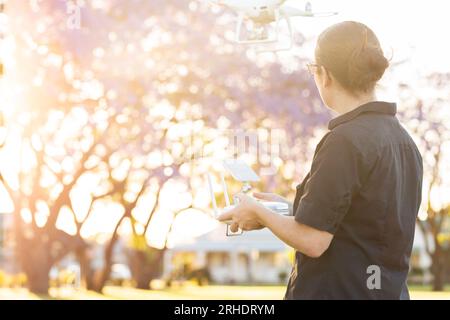 Giovane uomo d'affari che vola con un drone RPA al tramonto vicino a alberi in fiore viola Foto Stock