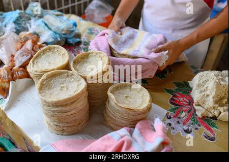 Cuoco anonimo con un alto angolo di raccolto vicino alle tortillas appena fatte sul bancone nel tipico negozio messicano Foto Stock